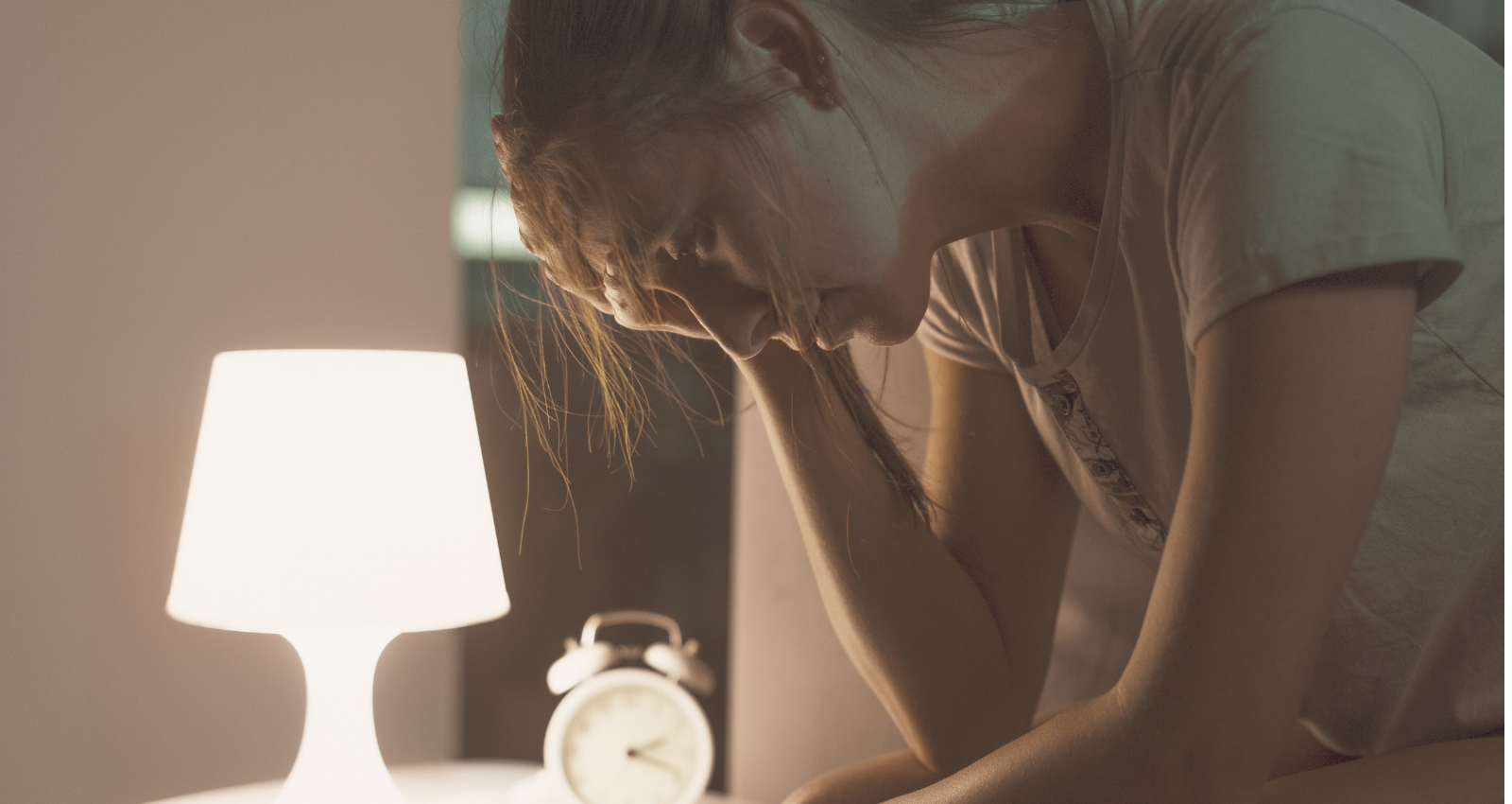 woman with head in her hands, tired. In a dimly lit bedroom with a night light on and an alarm clock