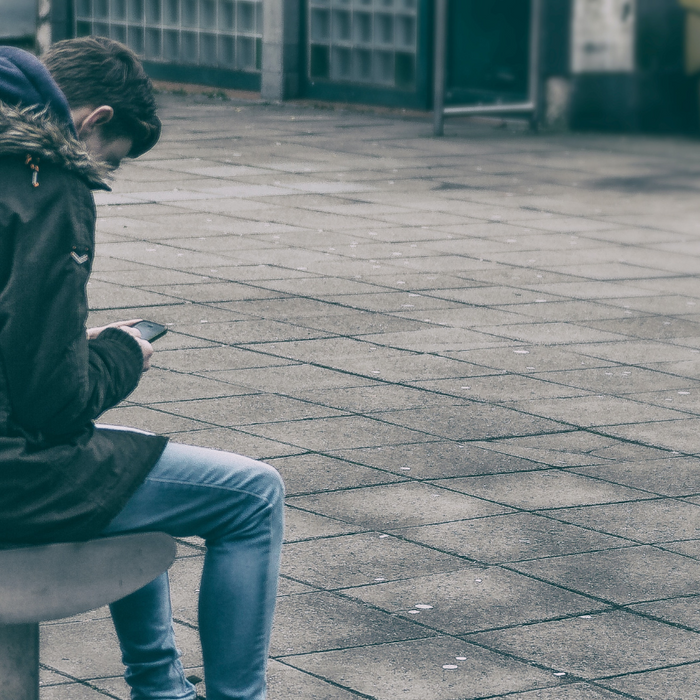boy sitting on a bench bent over looking at their mobile phone