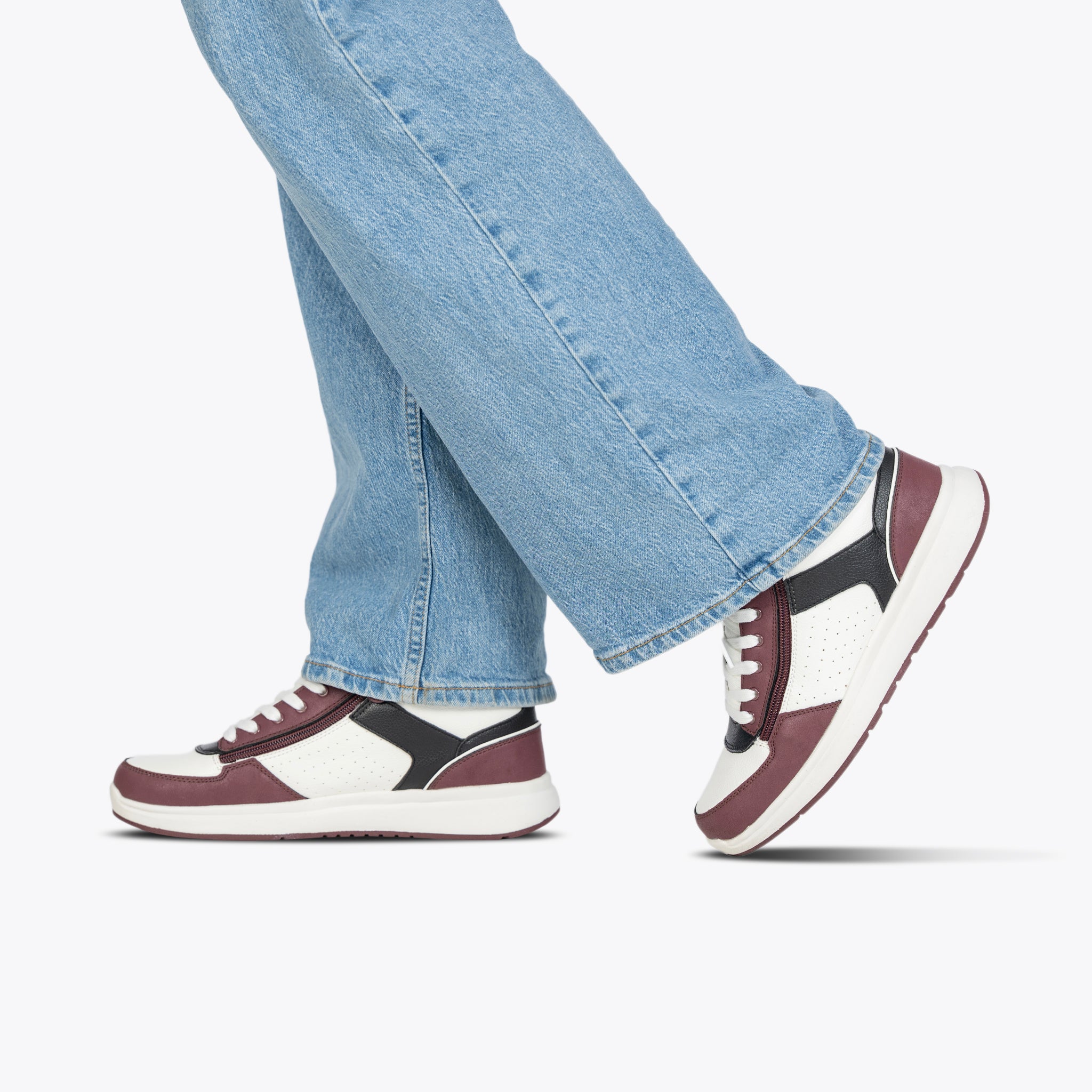 Person wearing maroon, black and white trainers with blue jeans on a white background